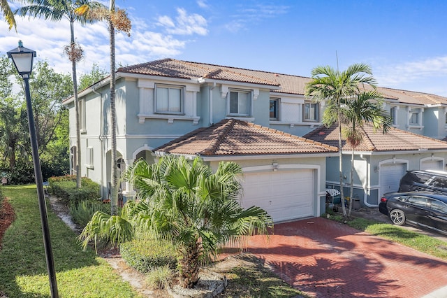 mediterranean / spanish-style home with decorative driveway, a tile roof, an attached garage, and stucco siding