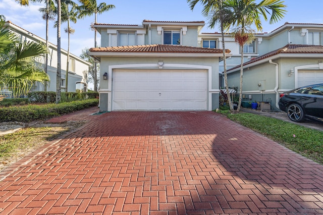 mediterranean / spanish house with decorative driveway, a tile roof, an attached garage, and stucco siding