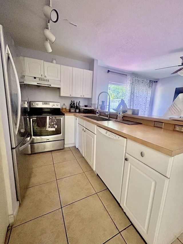 kitchen featuring light tile patterned floors, a peninsula, a sink, stainless steel appliances, and under cabinet range hood