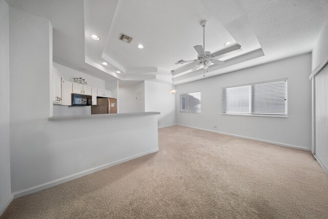 unfurnished living room with a tray ceiling, baseboards, visible vents, and light carpet