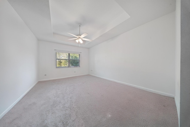 unfurnished room featuring a tray ceiling, carpet flooring, a ceiling fan, and baseboards