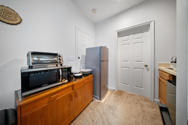 kitchen featuring stainless steel appliances, light carpet, brown cabinetry, and a toaster