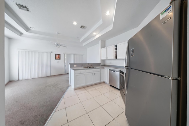 kitchen with a tray ceiling, stainless steel appliances, light carpet, and visible vents