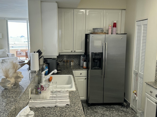 kitchen featuring dark stone counters, decorative backsplash, stainless steel fridge with ice dispenser, white cabinetry, and a sink