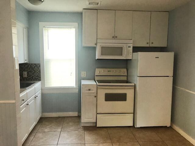 1831 Juno Rd Unit 123, North Palm Beach, FL 33408 - kitchen with white appliances, baseboards, light tile patterned floors, decorative backsplash, and white cabinetry