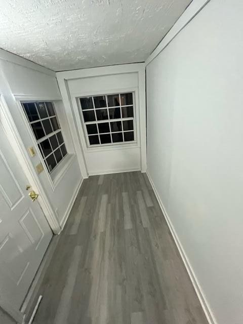 hall with dark wood finished floors, a textured ceiling, and baseboards