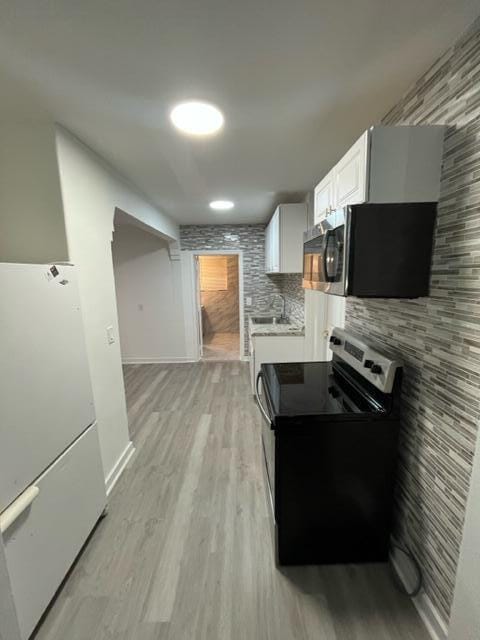 kitchen with baseboards, light wood-type flooring, stainless steel appliances, white cabinetry, and a sink