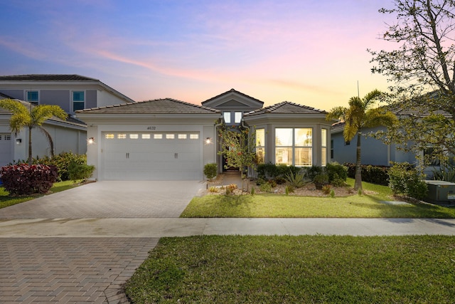 view of front facade featuring a garage, stucco siding, decorative driveway, and a yard