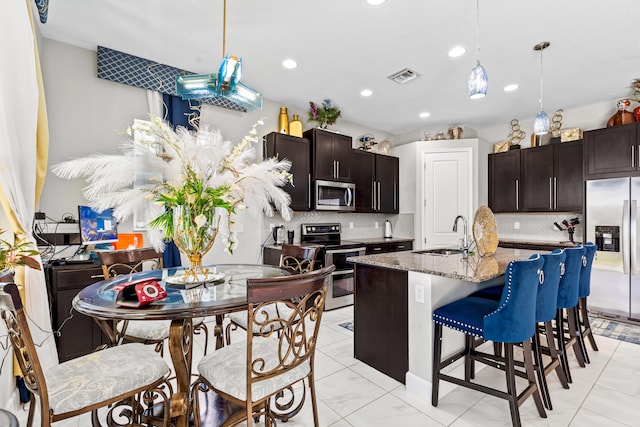 kitchen with a breakfast bar area, visible vents, a sink, stainless steel appliances, and backsplash