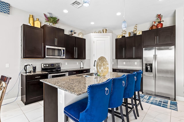 kitchen with visible vents, a kitchen bar, a sink, light stone counters, and appliances with stainless steel finishes