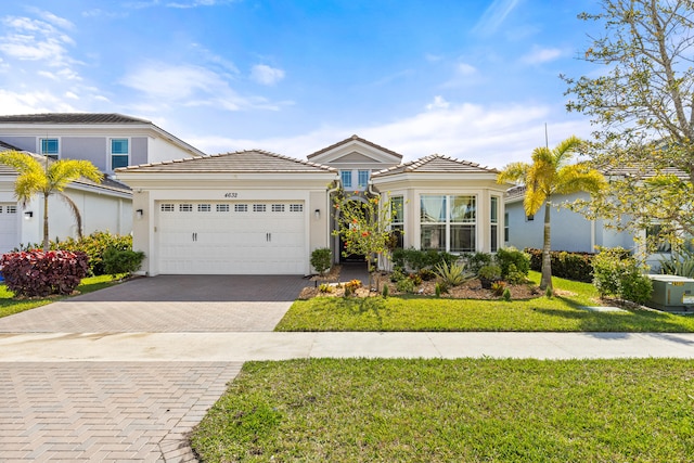 view of front of property featuring stucco siding, decorative driveway, a front yard, a garage, and a tiled roof