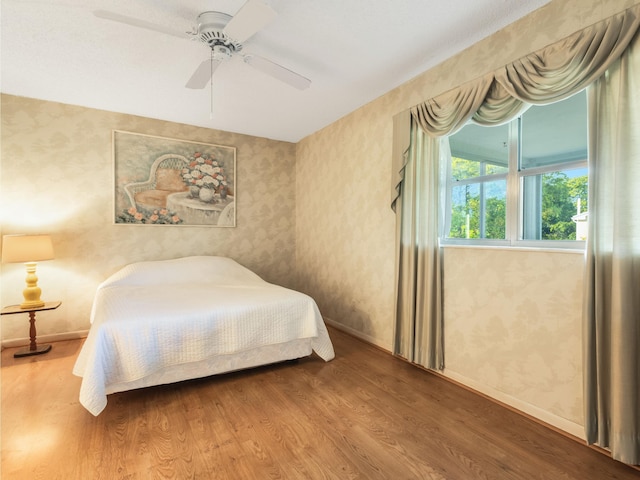 bedroom with baseboards, wood finished floors, a ceiling fan, and wallpapered walls