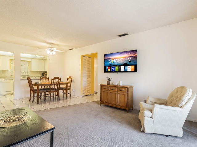 living area featuring light tile patterned floors, visible vents, light colored carpet, and a ceiling fan