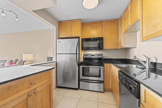 kitchen with light tile patterned floors, stainless steel appliances, dark stone counters, and a sink