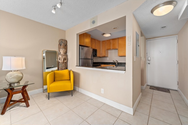 kitchen with a textured ceiling, freestanding refrigerator, arched walkways, light tile patterned floors, and baseboards