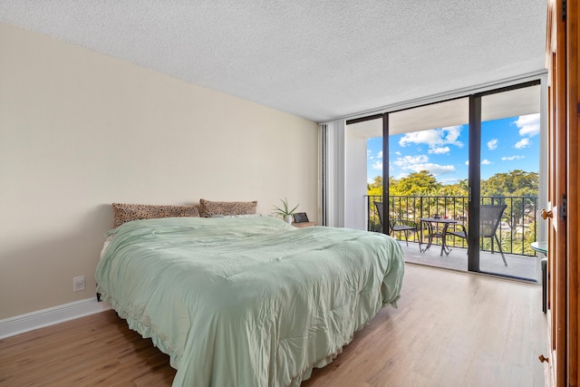 bedroom with expansive windows, baseboards, a textured ceiling, access to outside, and light wood-type flooring