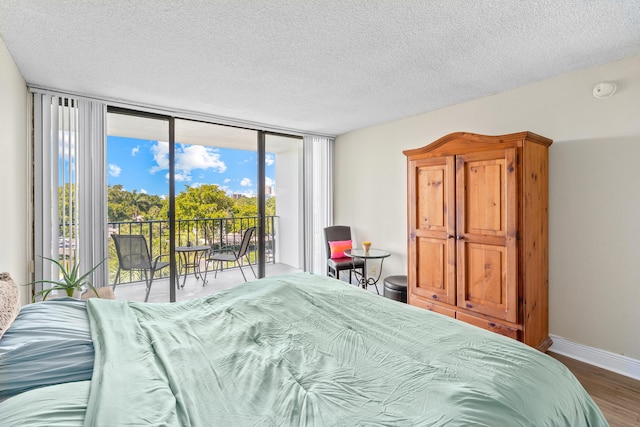 bedroom featuring access to exterior, baseboards, a wall of windows, wood finished floors, and a textured ceiling