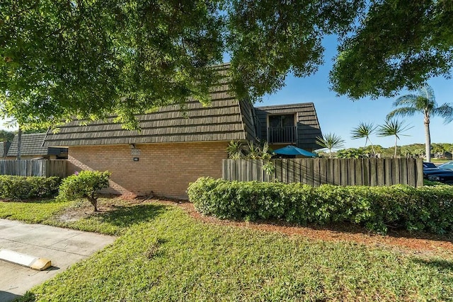 exterior space featuring a yard, fence, mansard roof, and brick siding