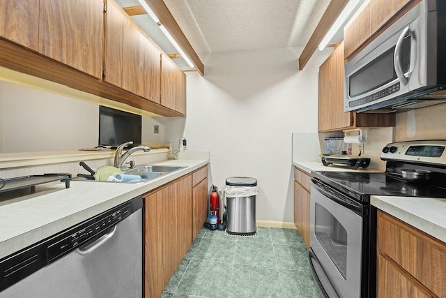 kitchen with light countertops, appliances with stainless steel finishes, a sink, a textured ceiling, and baseboards