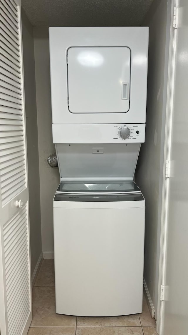 washroom featuring laundry area, stacked washer / dryer, light tile patterned floors, and baseboards