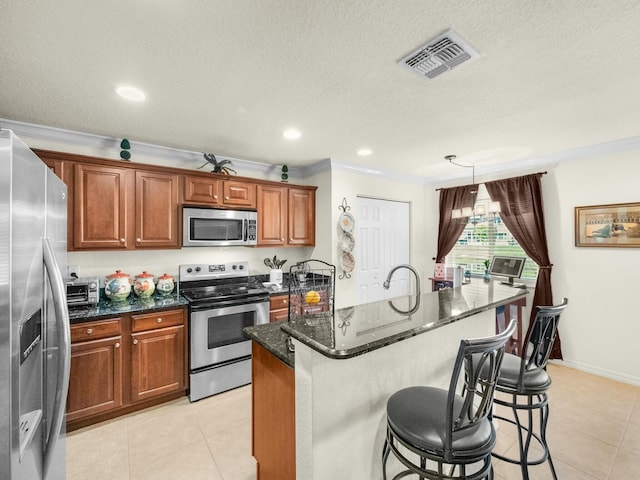 kitchen featuring light tile patterned floors, a center island with sink, visible vents, stainless steel appliances, and a kitchen breakfast bar