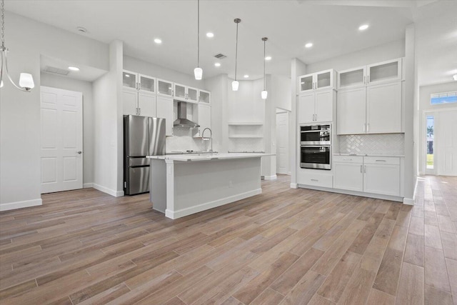 kitchen with stainless steel appliances, light wood-style floors, decorative backsplash, wall chimney range hood, and light countertops