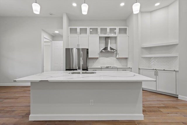 kitchen with freestanding refrigerator, wall chimney range hood, white cabinetry, and decorative backsplash