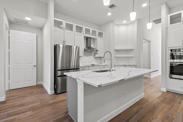 kitchen with wall chimney range hood, a sink, appliances with stainless steel finishes, dark wood-type flooring, and visible vents