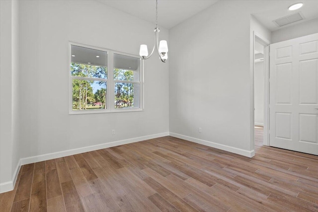 unfurnished dining area with baseboards, a chandelier, wood finished floors, and visible vents