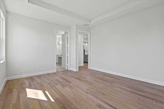 unfurnished bedroom featuring light wood-style flooring, baseboards, and connected bathroom