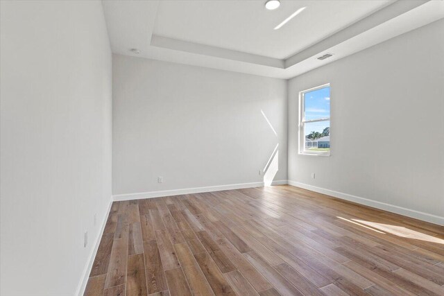 spare room with a tray ceiling, wood finished floors, visible vents, and baseboards