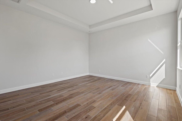 unfurnished room with baseboards, wood finished floors, and a raised ceiling