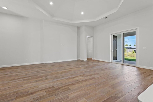 empty room with light wood-style floors, a tray ceiling, baseboards, visible vents, and recessed lighting