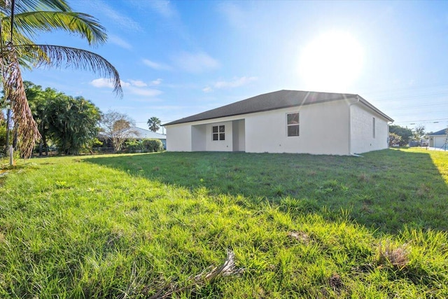 rear view of house featuring a yard and stucco siding