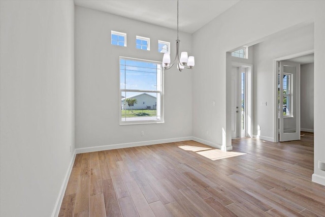 unfurnished dining area with an inviting chandelier, baseboards, and wood finished floors