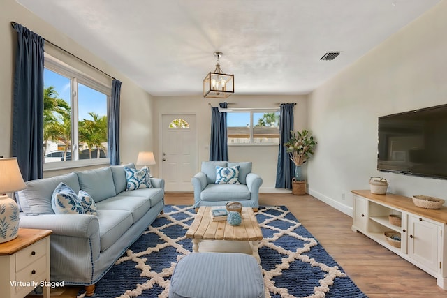 living room with visible vents, a healthy amount of sunlight, light wood-type flooring, and a chandelier
