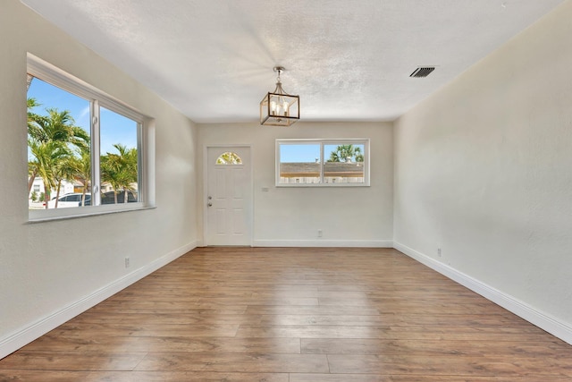 unfurnished room with plenty of natural light, a notable chandelier, and hardwood / wood-style flooring