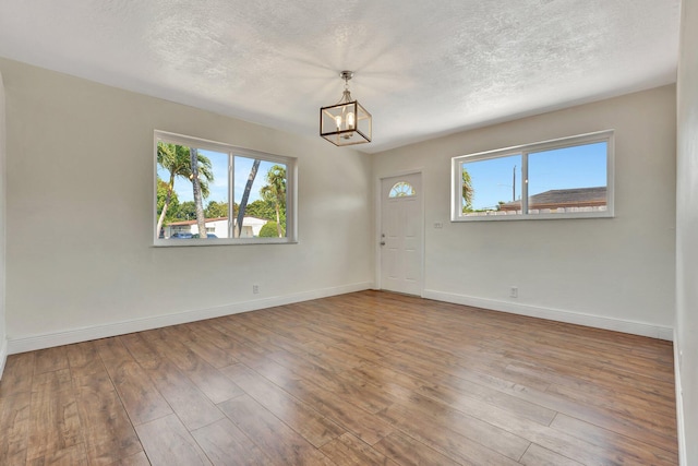 foyer entrance with baseboards, a notable chandelier, a healthy amount of sunlight, and wood finished floors