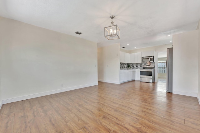 unfurnished living room with an inviting chandelier, baseboards, visible vents, and light wood finished floors