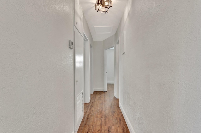 hallway with wood finished floors, baseboards, and a textured wall