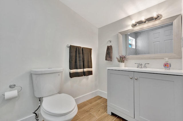 bathroom with baseboards, wood tiled floor, toilet, vaulted ceiling, and vanity