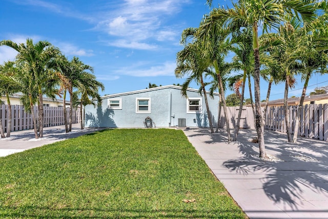 view of front of house with a front lawn, fence, central AC, and stucco siding