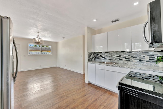 kitchen with visible vents, backsplash, light wood-style flooring, stainless steel appliances, and a sink