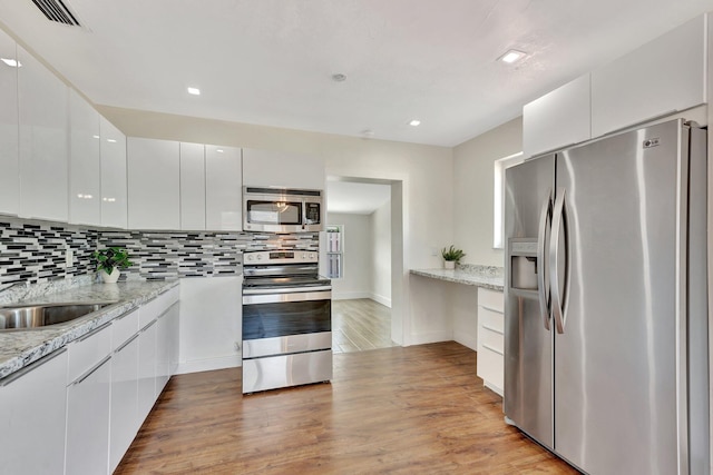 kitchen with backsplash, light wood-style flooring, stainless steel appliances, and modern cabinets