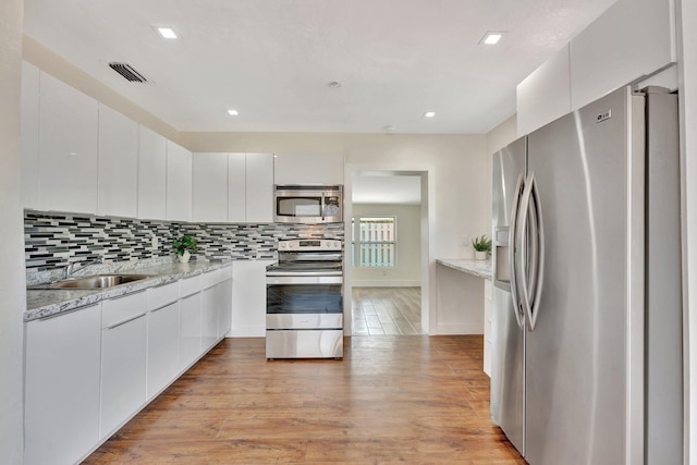 kitchen with light wood-type flooring, decorative backsplash, appliances with stainless steel finishes, modern cabinets, and a sink