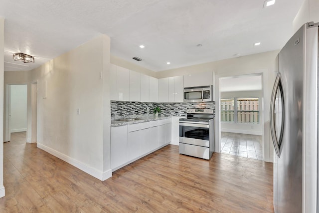 kitchen featuring visible vents, light wood finished floors, stainless steel appliances, white cabinetry, and backsplash