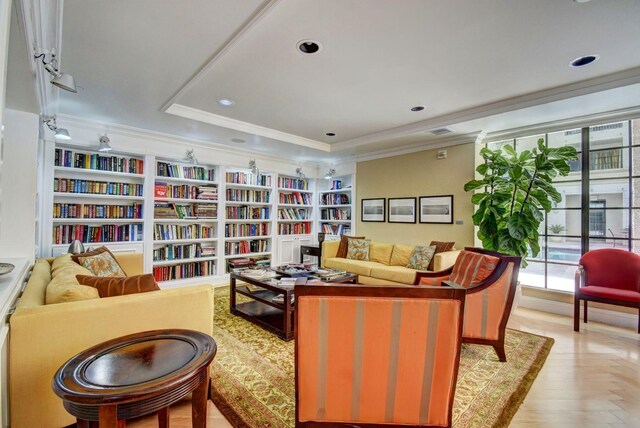 sitting room featuring built in shelves, recessed lighting, a raised ceiling, bookshelves, and ornamental molding