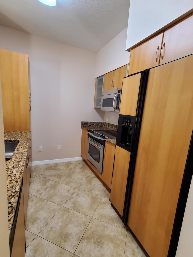 kitchen featuring stainless steel appliances, baseboards, dark stone countertops, and light tile patterned floors