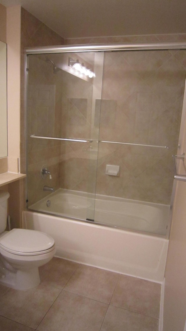 bathroom featuring toilet, tile patterned flooring, and bath / shower combo with glass door