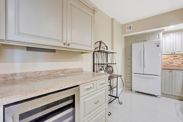 kitchen with visible vents, backsplash, freestanding refrigerator, wine cooler, and light stone countertops